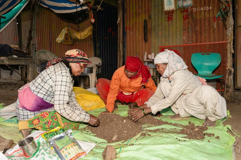 Three women in traditional attire working with soil in a rural setting in Nagpur, India.